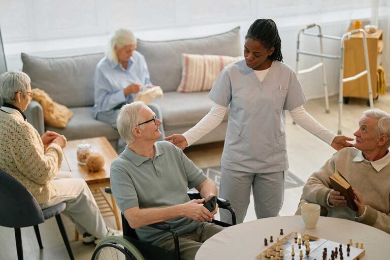 An older adult sitting with a tablet, discussing paperwork with a family member at a kitchen table.