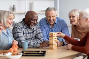 Older adults share a meal and conversation in a bright assisted living dining room with staff nearby.