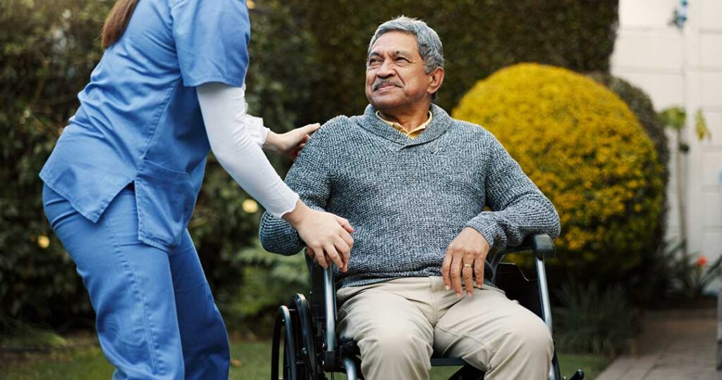 Older adult smiling and unpacking personal items in a cozy, sunlit senior living apartment with a visiting family member.